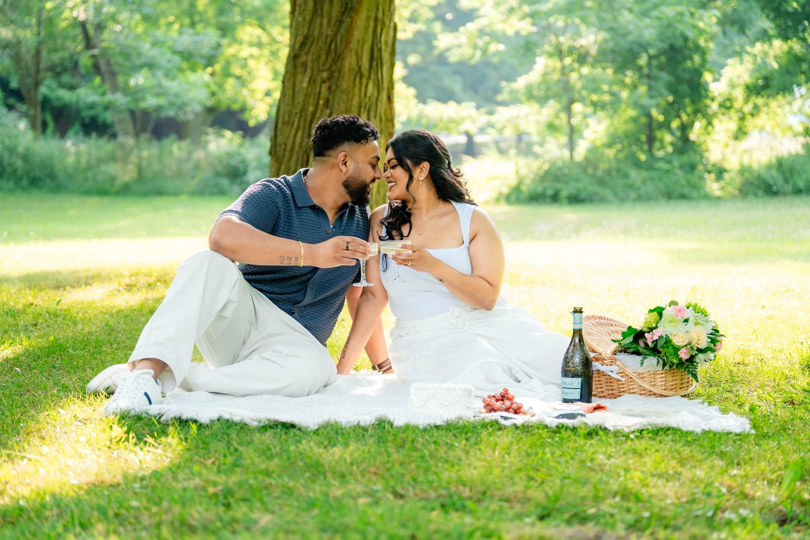 Piratheepan and Shivanna at a golden-hour picnic with a wicker basket and champagne set out on a blanket