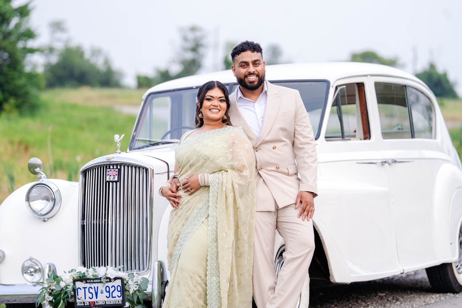 Shivanna in a sage-green traditional saree standing beside a vintage white Rolls Royce on a rural road
