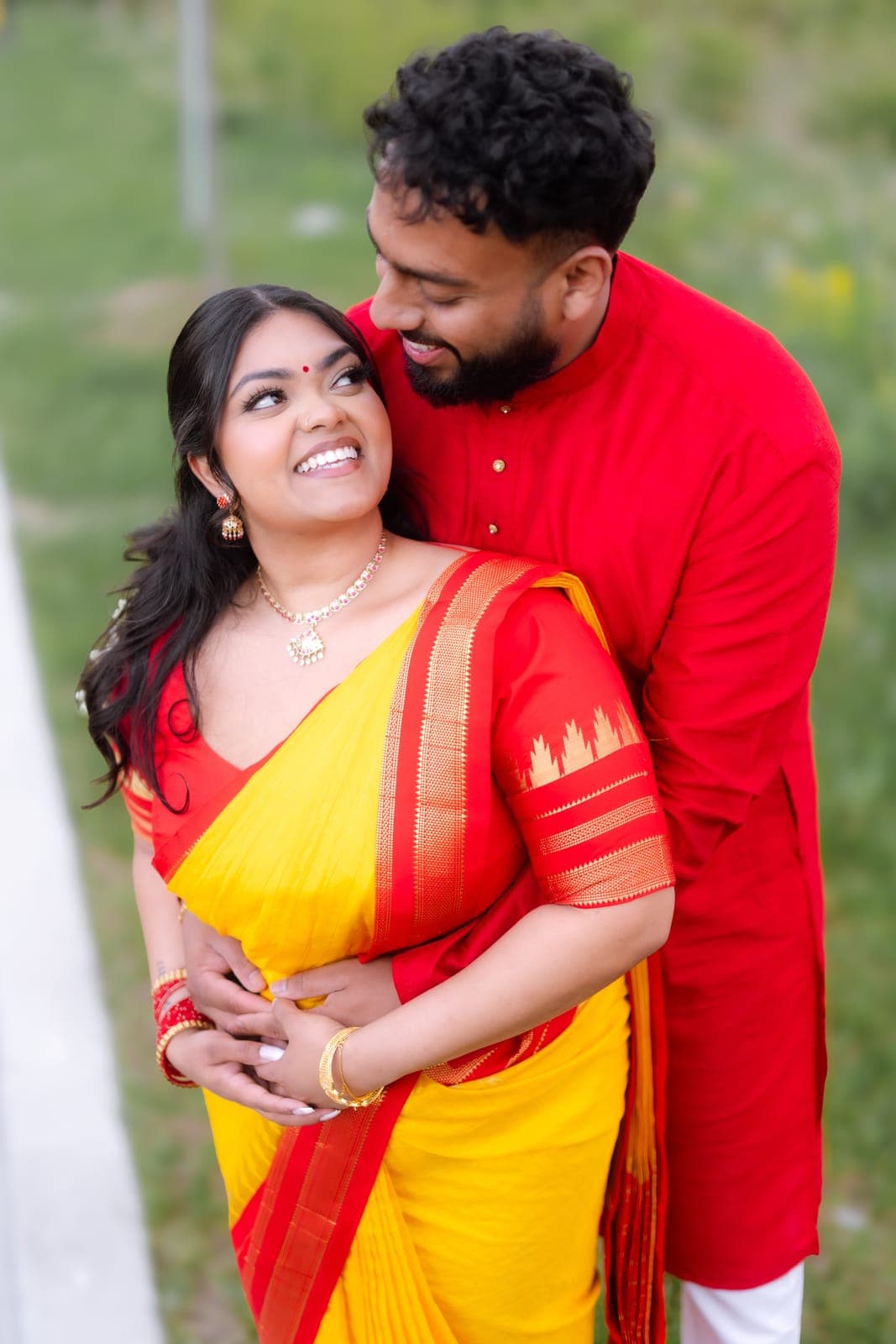 Close-up of Piratheepan and Shivanna in red and yellow traditional outfits, outdoors on a sunlit lawn